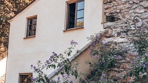 A two-story building with a stone staircase leading to the entrance, surrounded by potted plants and flowers. - Le Petit Chateau (Vezzi Portio)