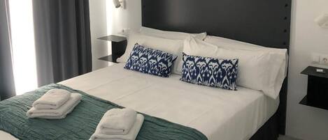 A modern hotel room with a large bed, dark headboard, and two patterned pillows.