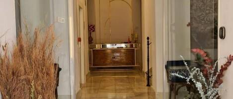 Un vestíbulo de hotel con entrada por puerta de vidrio, una recepción y un comedor visibles a través del vidrio.