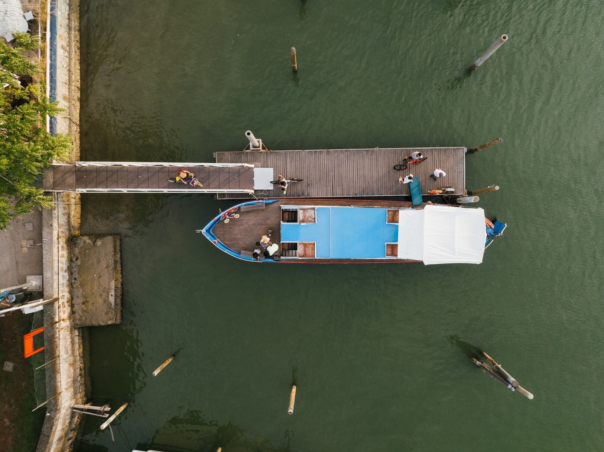 A boat docked at a pier with a blue deck and a white awning, surrounded by calm water.
