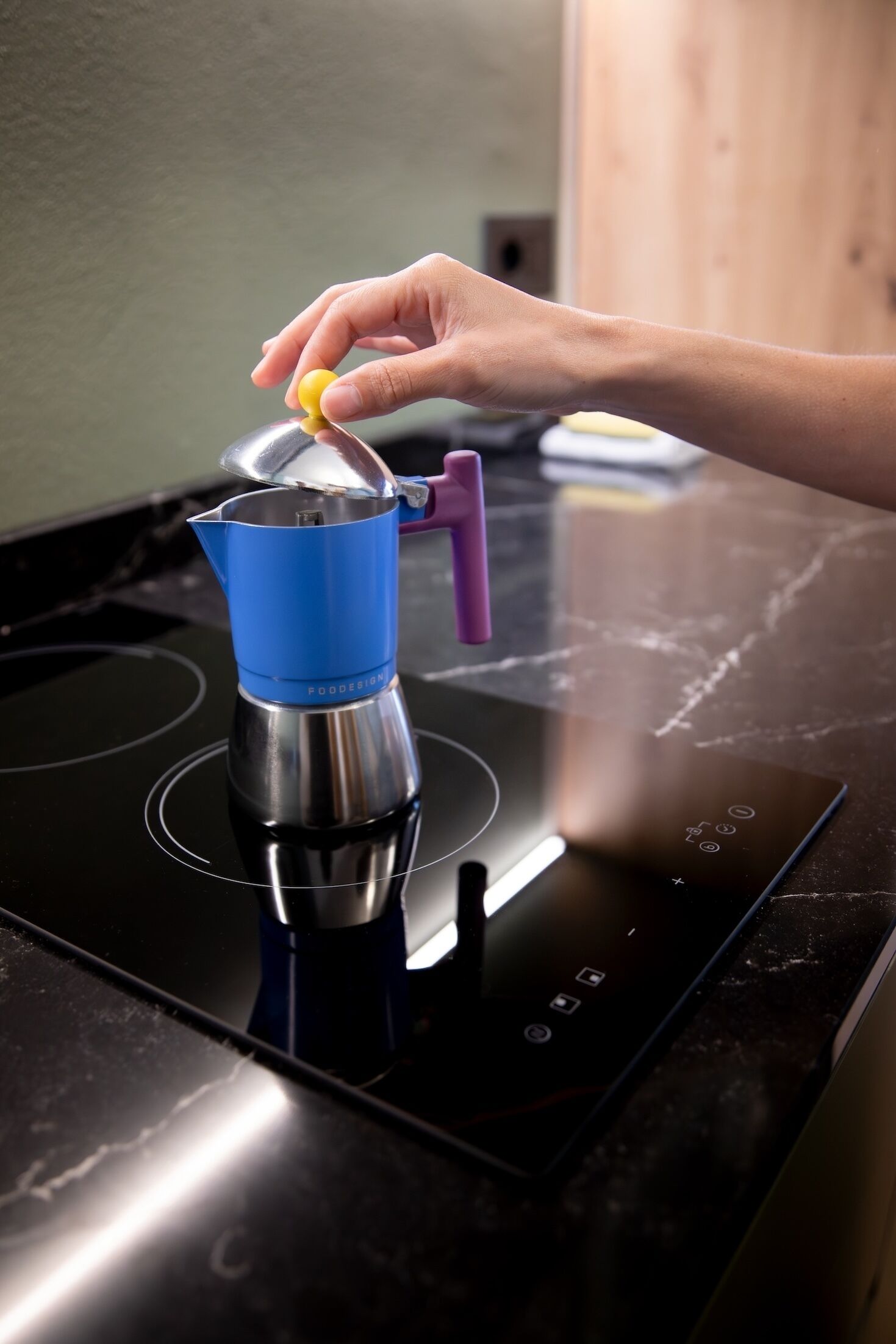 A hand placing a lid on a coffee pot on an induction cooktop.