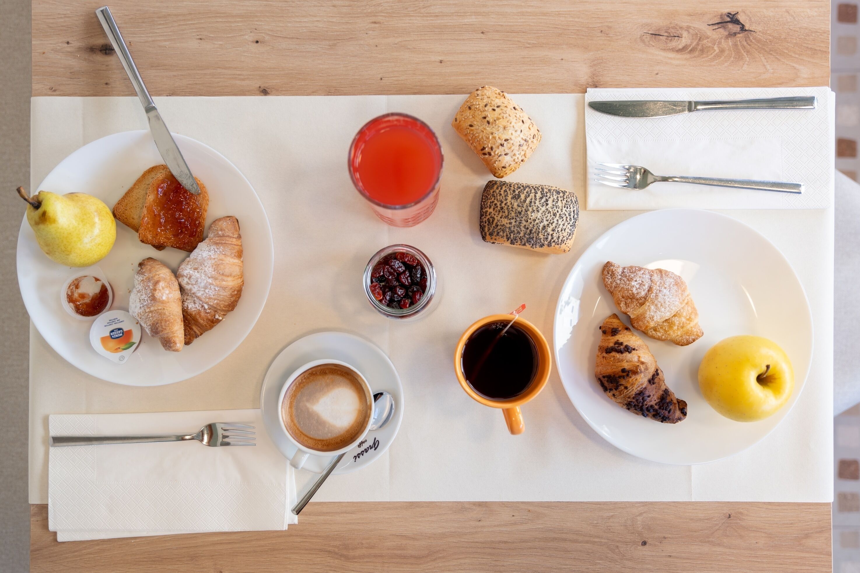 A breakfast setting with plates of food, a glass of juice, a cup of coffee, and cutlery on a wooden table.