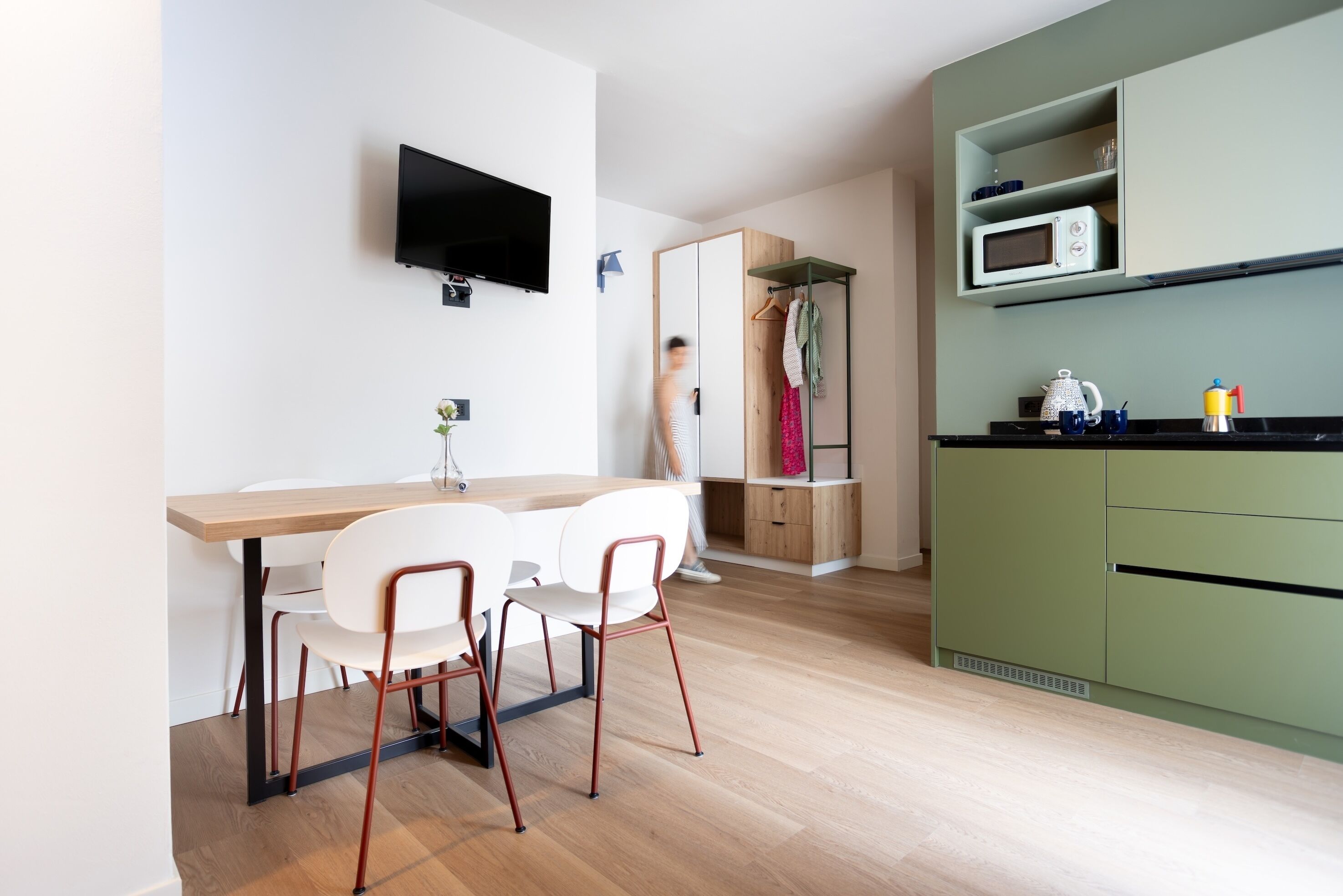 Eine moderne Küche mit einem Holzespeisetisch und -stühlen, einem an der Wand montierten Flachbildfernseher und einem grünen Schrank mit einer Mikrowelle.