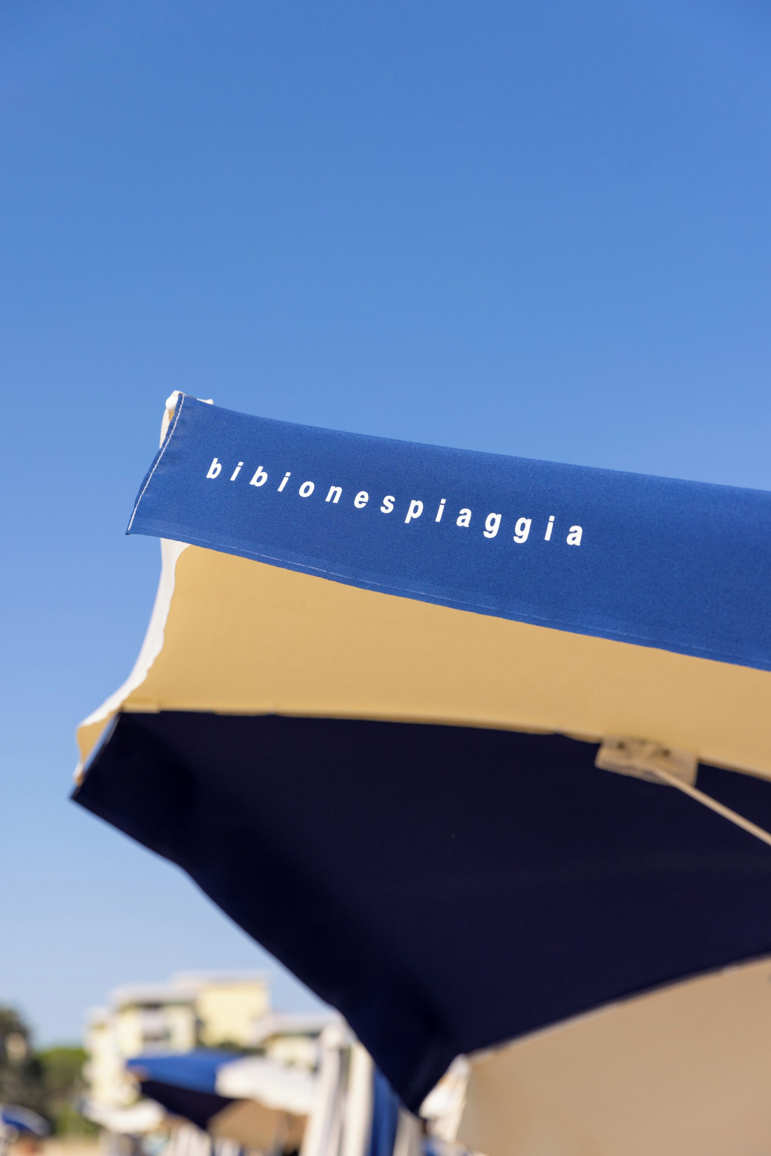 A blue and beige umbrella with the text 'bibonespia' on it.