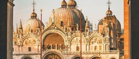 A grand building with multiple domes and arches, likely a historical or religious site, with a spacious plaza in front.