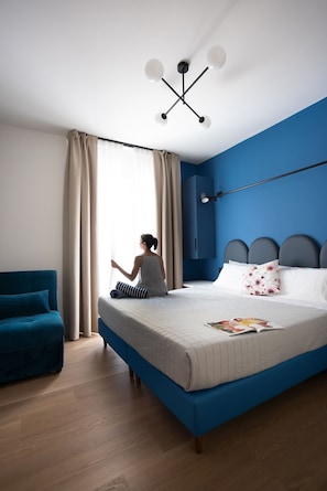 Ein Schlafzimmer mit einem Bett, einem blauen Sofa, einem Fenster mit Vorhängen und einer Deckenleuchte.