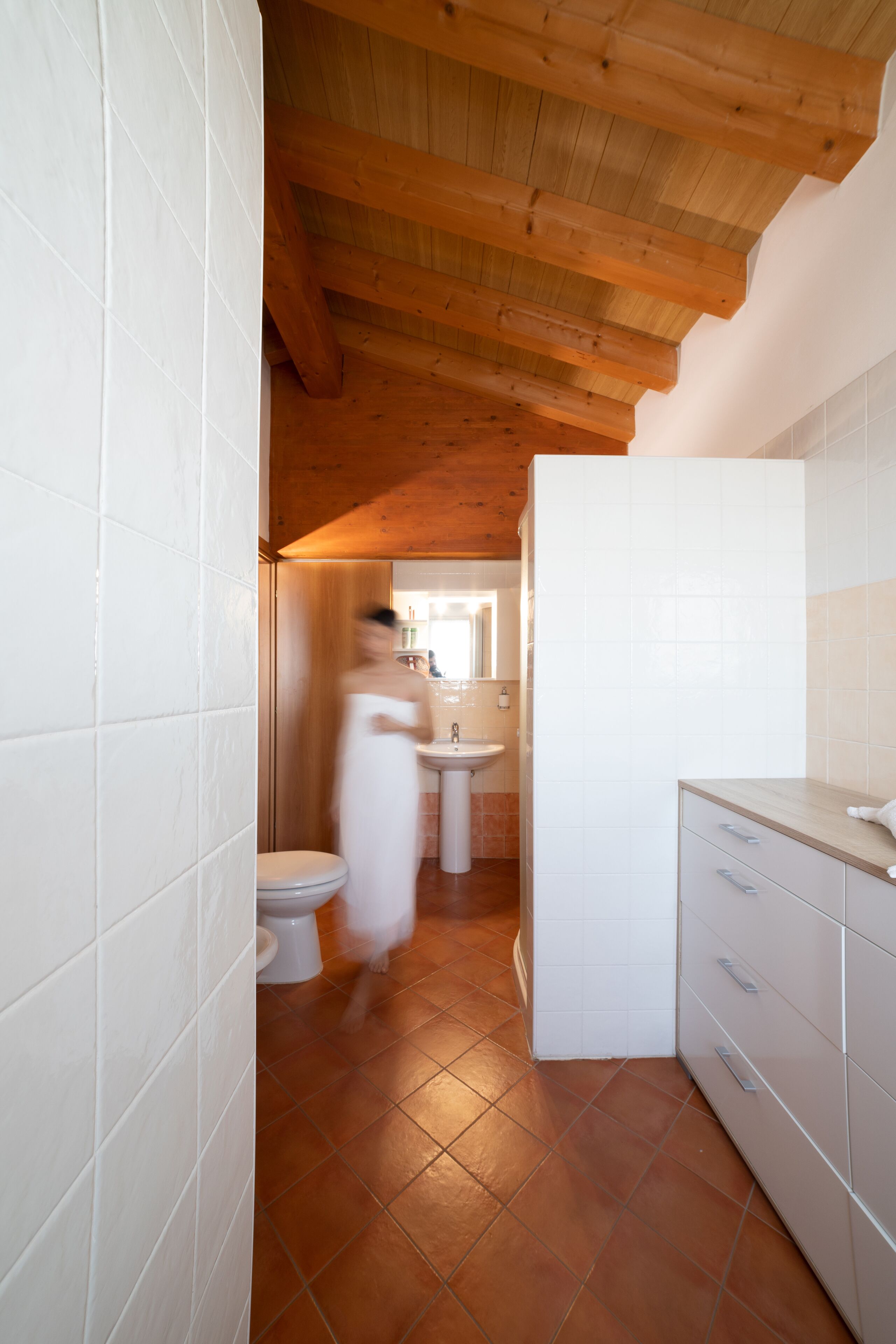 Een badkamer met witte tegels, een houten plafond, een wastafel en een toilet.
