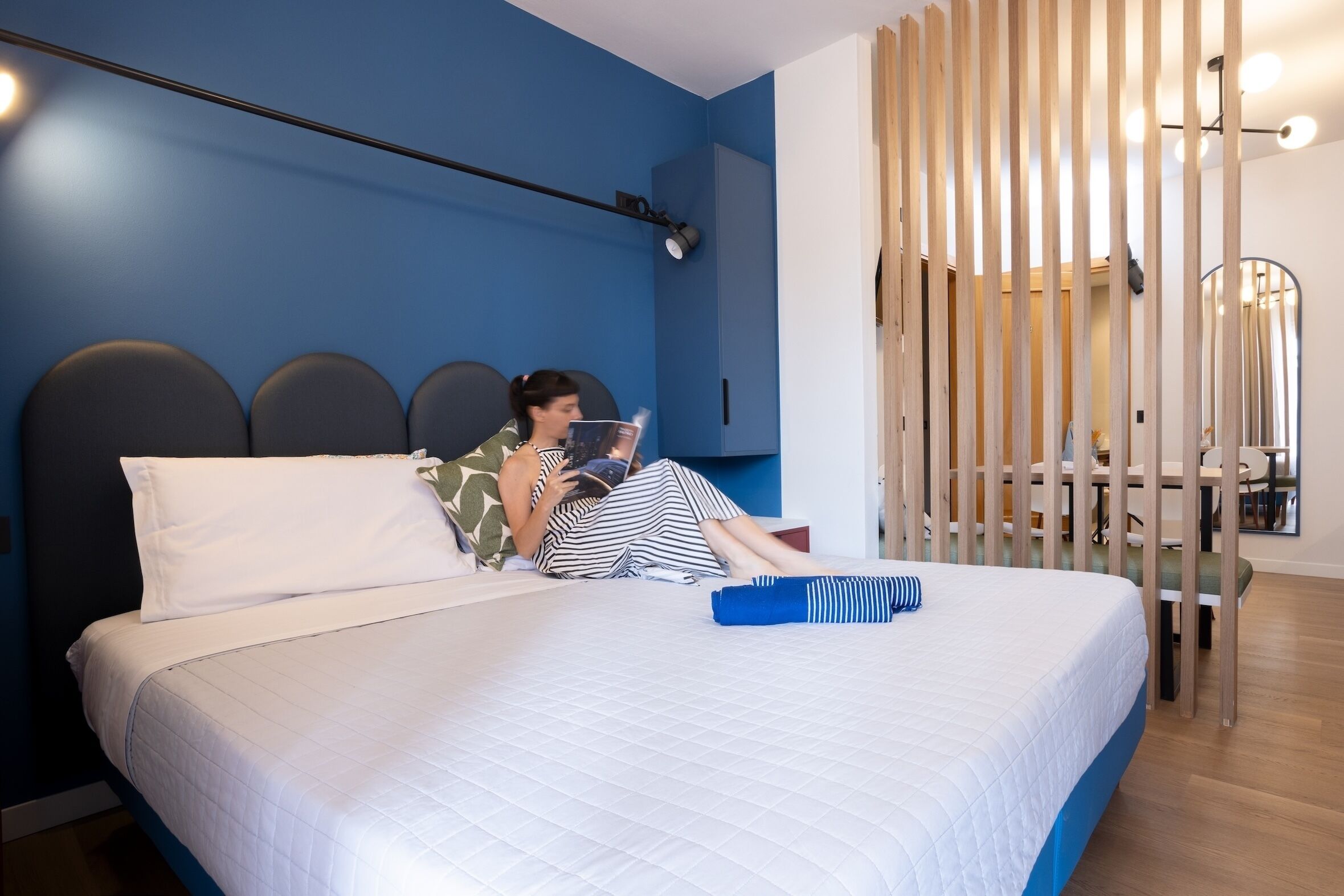 A bed with a white quilted bedspread, a person lying on it, and a blue wall in the background.