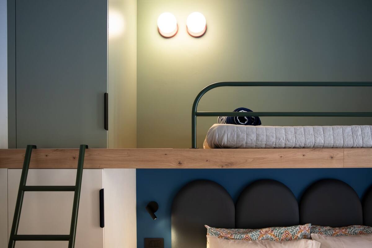 Un letto a castello con una scala, una testiera con decorazioni circolari e due luci fissate al muro.