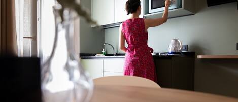 A person in a patterned dress reaching for a microwave in a kitchen with a sink and a kettle.