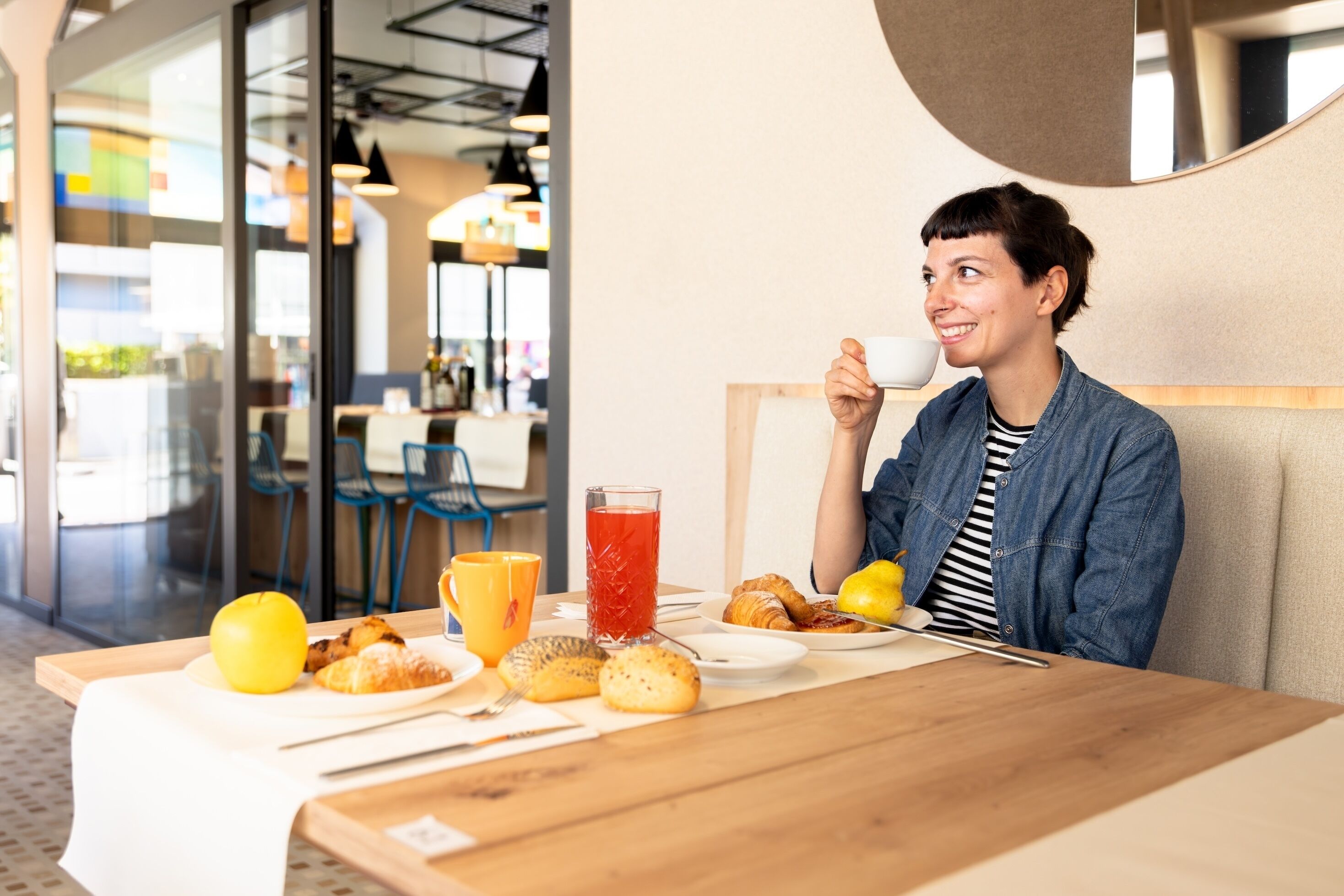 Una persona sentada a una mesa con alimentos para el desayuno, incluyendo cruasanes, una manzana y un vaso de jugo de cereza.
