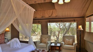 A bedroom with a bed, a sofa, two armchairs, a small table, and a lamp. - Safari Plains (Bela-Bela)