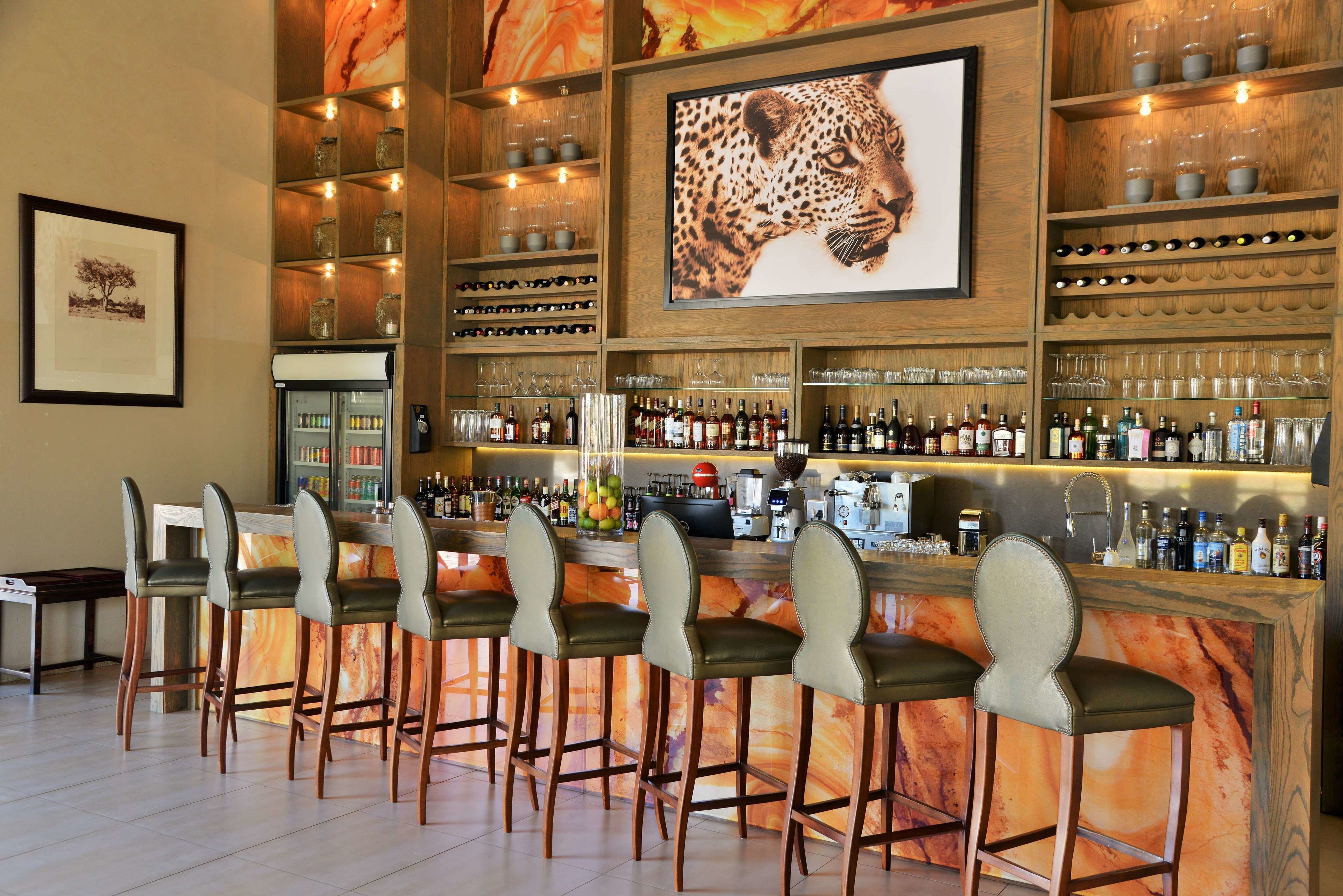 A bar area with a marble countertop, multiple shelves with bottles and glasses, and a large leopard print artwork on the wall.