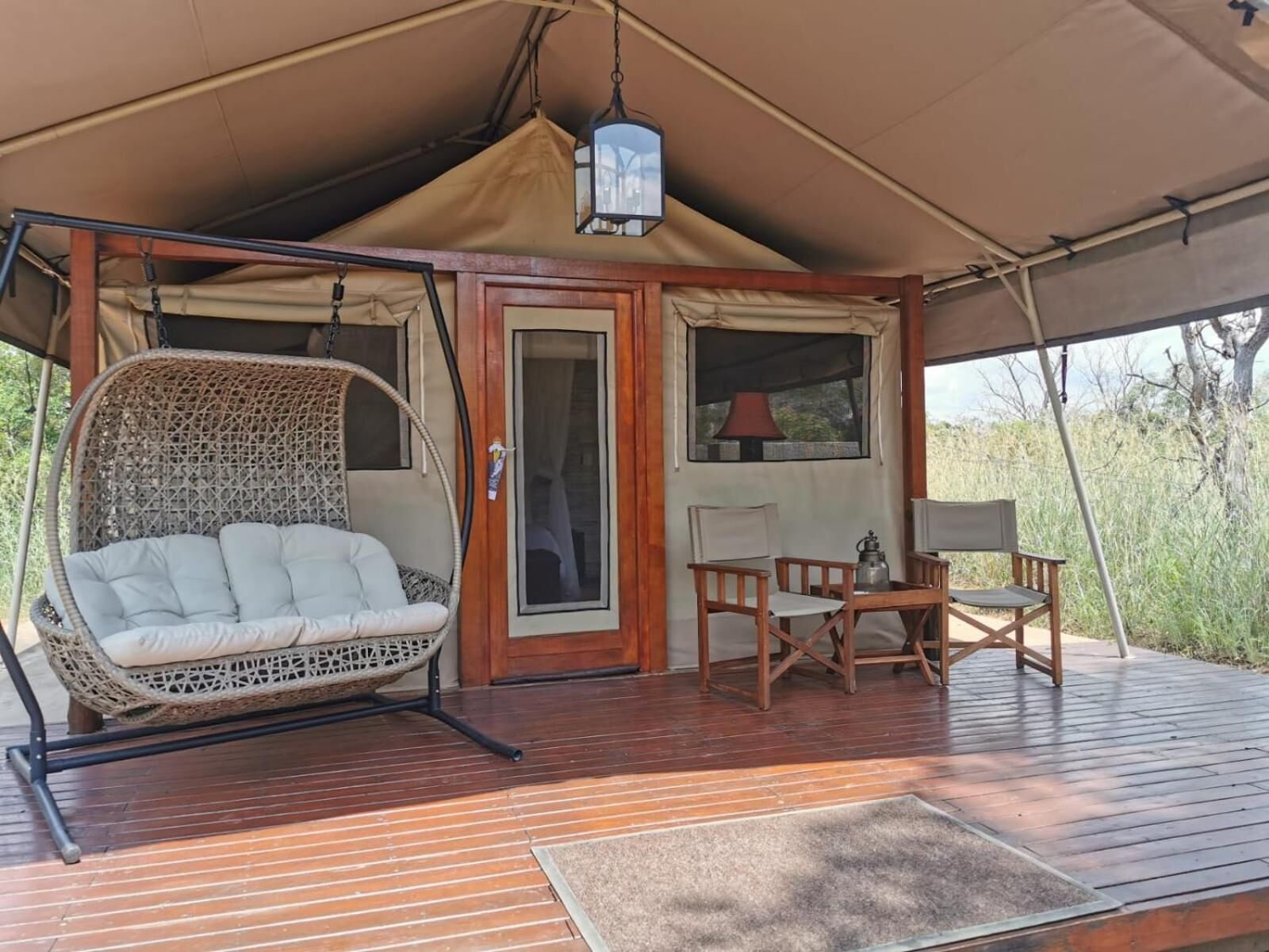 Alojamiento con carpa, una silla mecedora de mimbre, una mesa de madera y sillas.