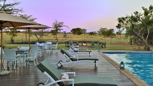 A poolside area with lounge chairs, a dining table, and a fire pit. - Safari Plains (Bela-Bela)