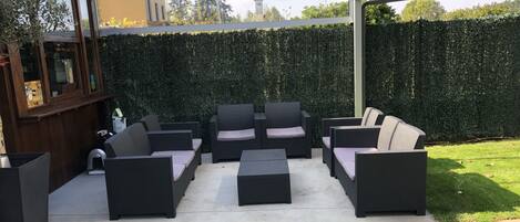 Un área de patio al aire libre con pérgola, disposición de asientos y un muro de seto.