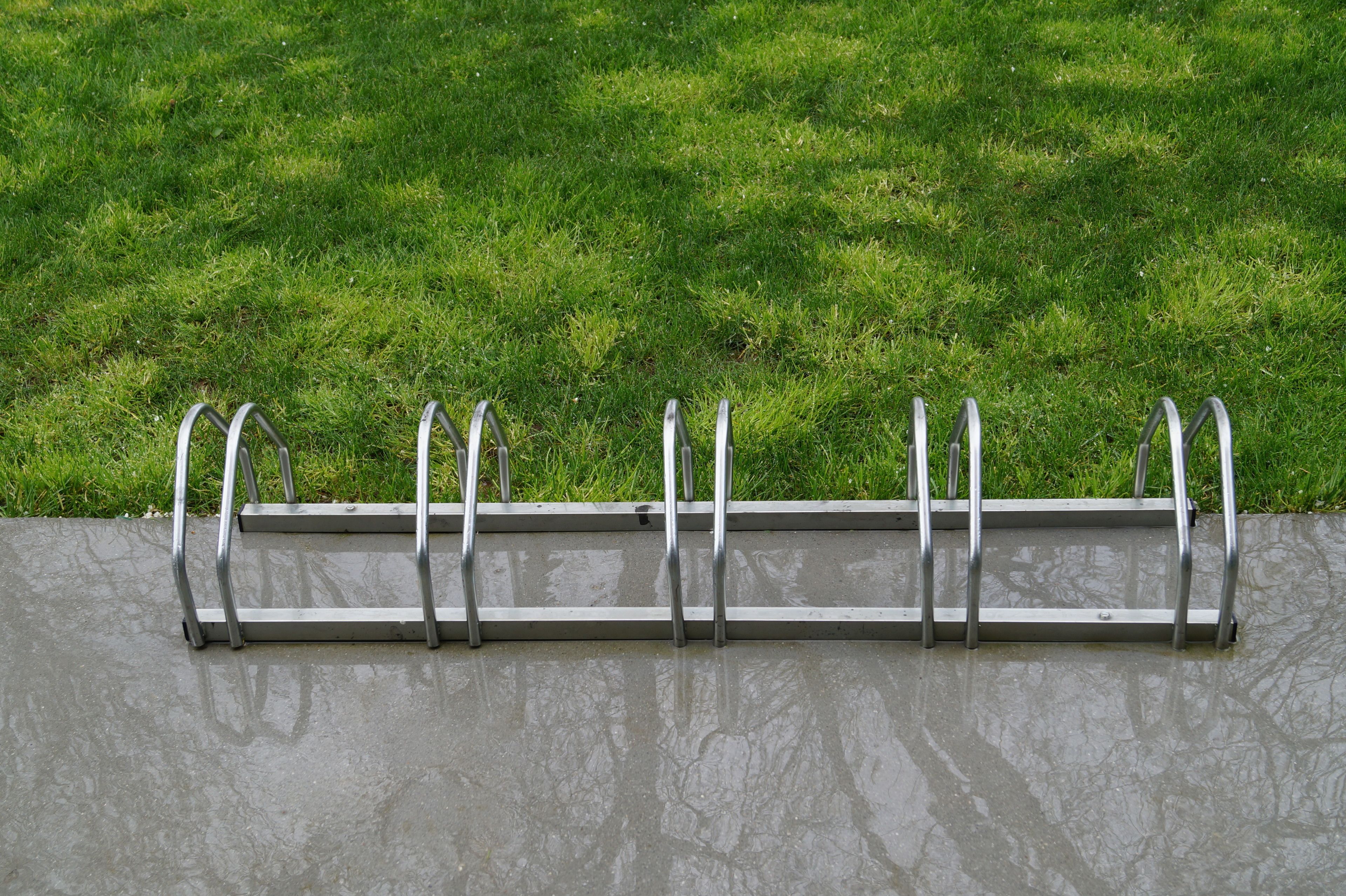 A metal bike rack attached to a concrete wall with a grassy background.