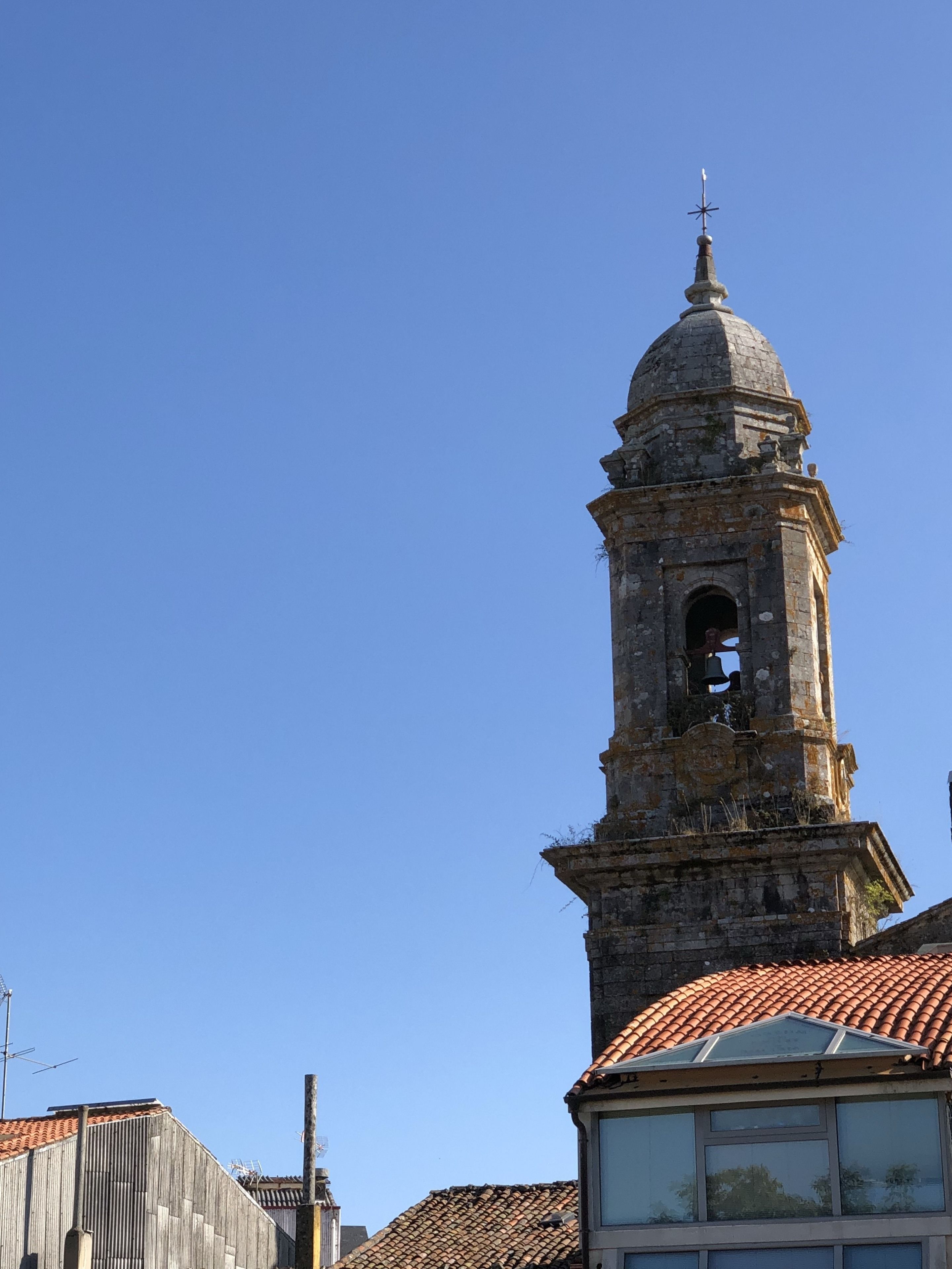 A historic bell tower with a dome and a cross on top, surrounded by buildings with tiled roofs.