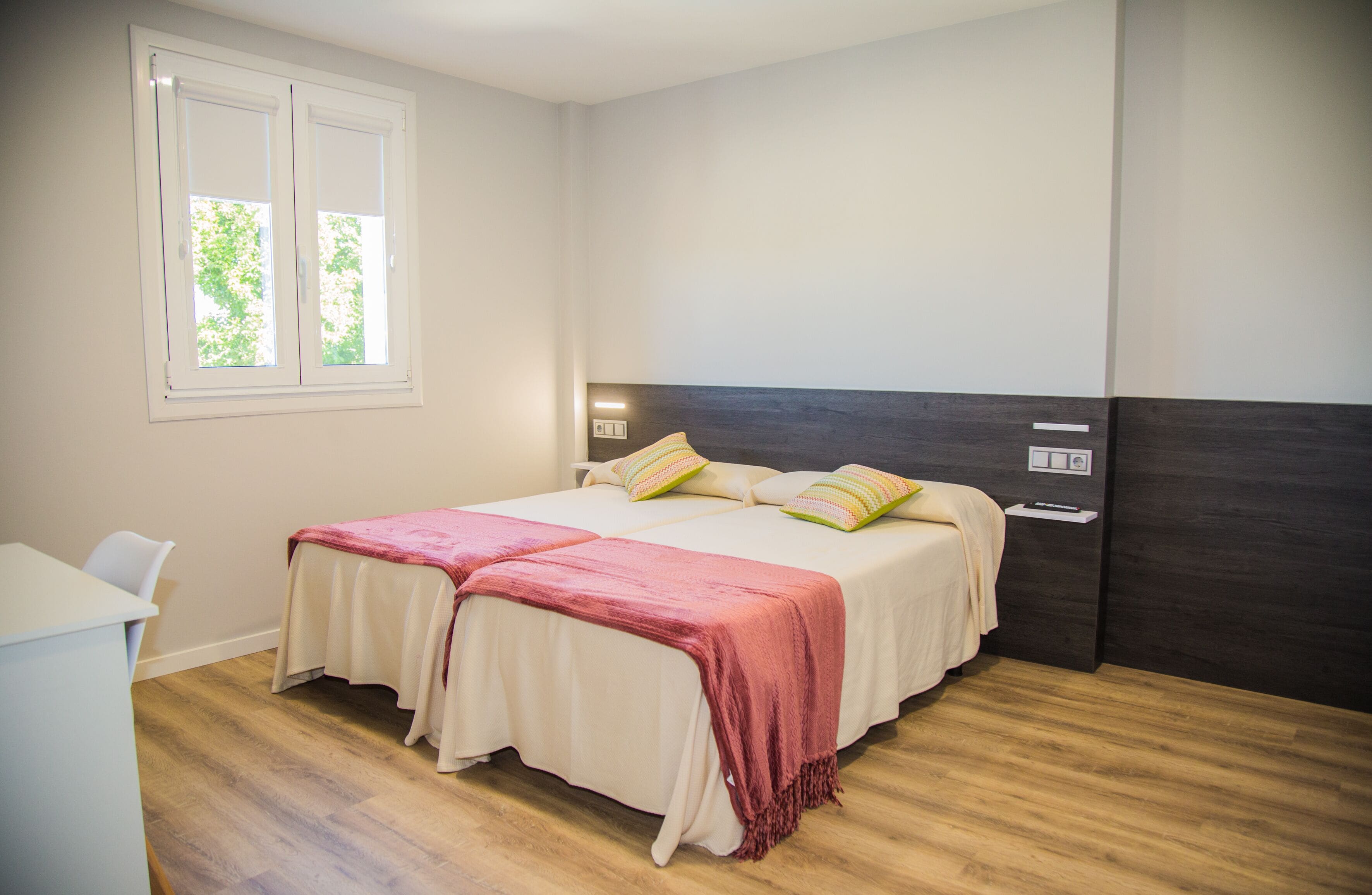 Un dormitorio con dos camas, un escritorio y una ventana que da a vistas de vegetación.