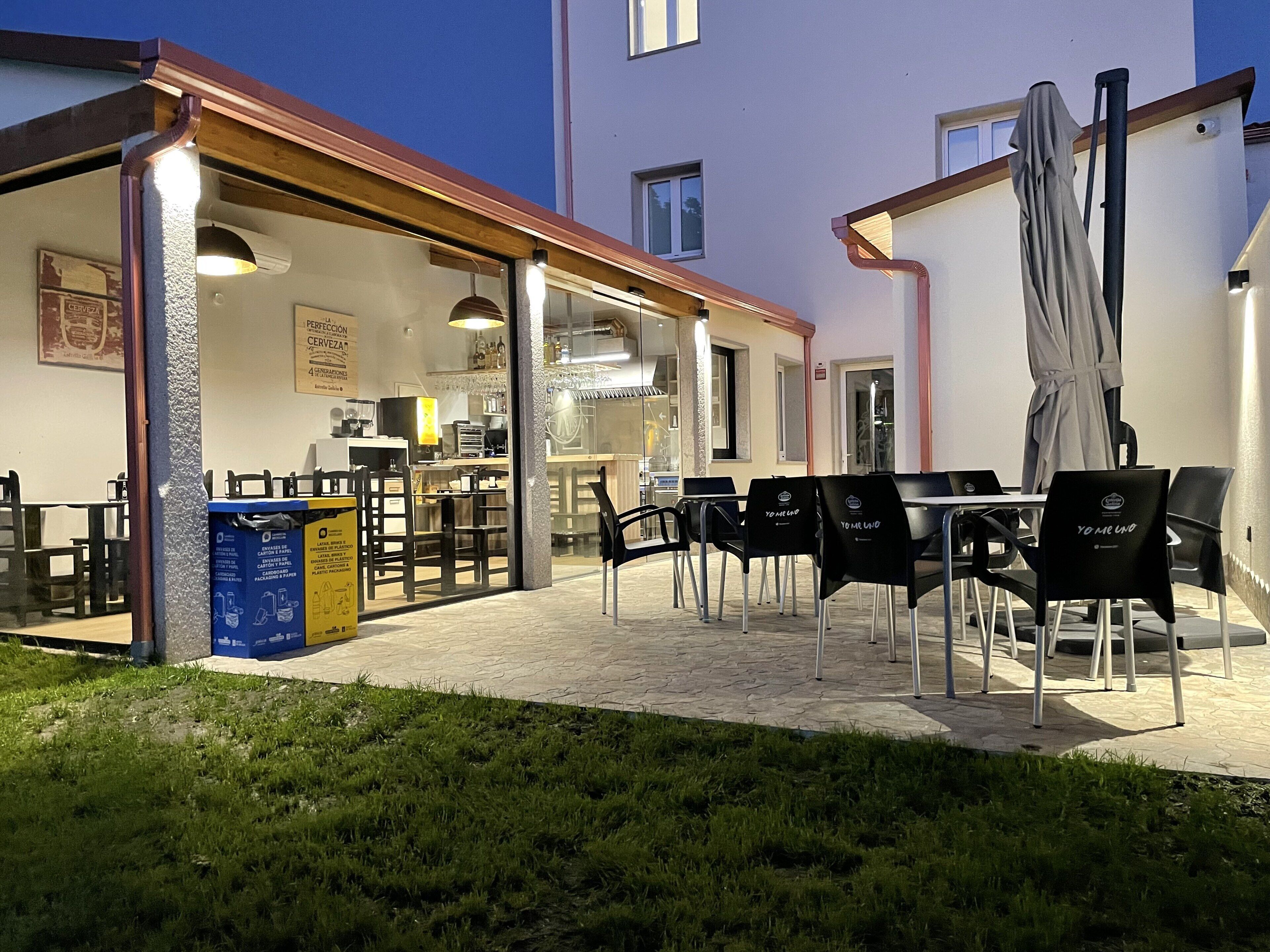 An outdoor patio area with tables and chairs, a covered seating area, and a building with a kitchen visible inside.