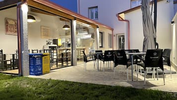 An outdoor patio area with tables and chairs, a covered seating area, and a building with a kitchen visible inside.
