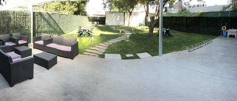 A patio area with outdoor furniture, a hedge, and a concrete path.