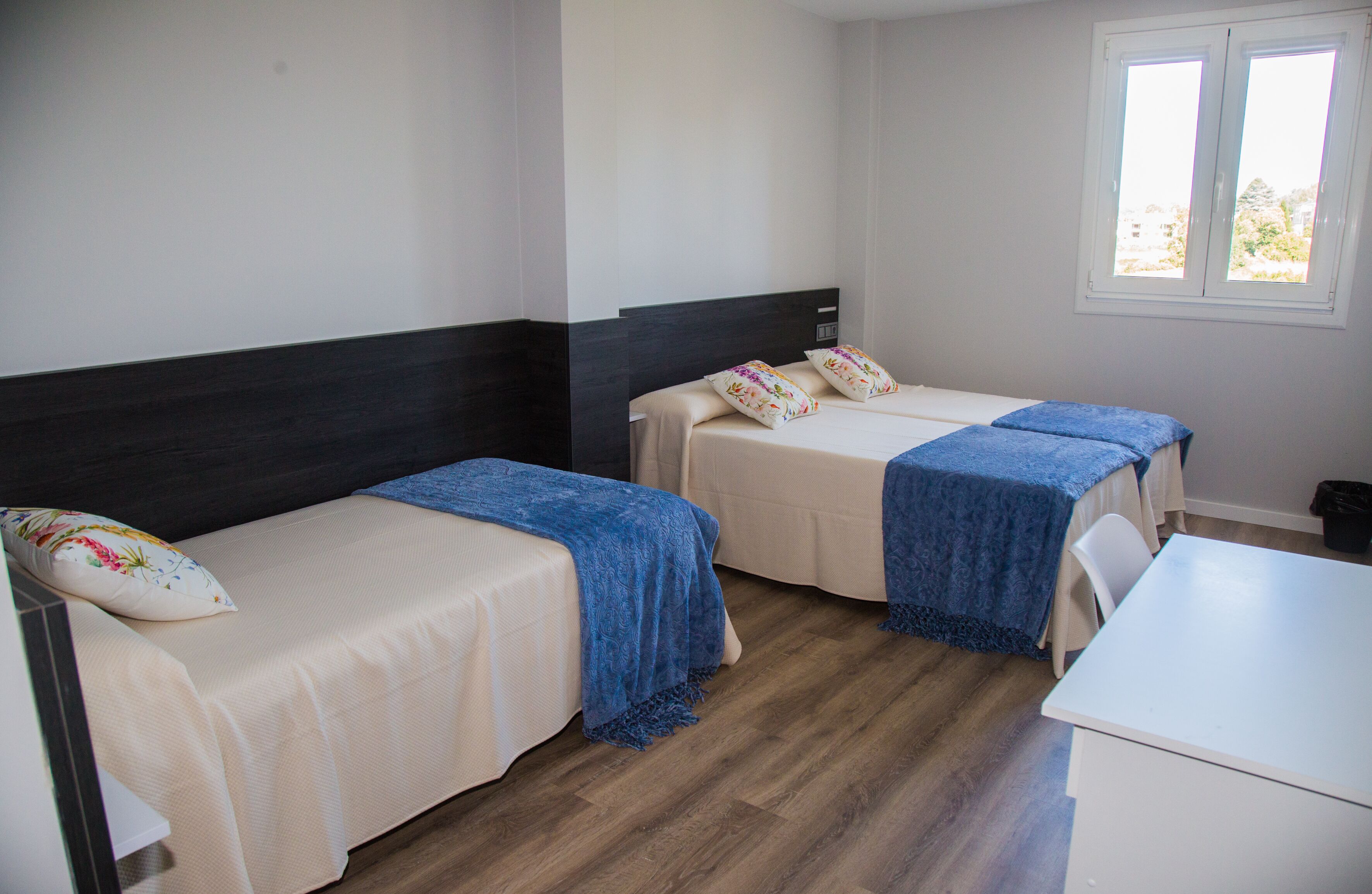 A hotel room with two beds, a desk, and a window.