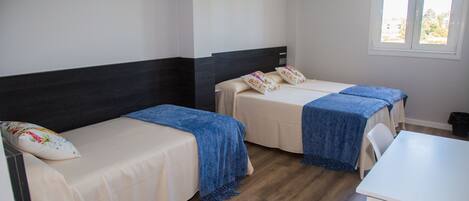 A hotel room with two beds, a desk, and a window.