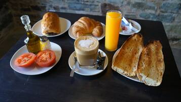 A breakfast setting with croissants, toast, tomatoes, a bottle of olive oil, a glass of orange juice, and a cup of coffee on a table.