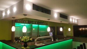 Zona de bar con mostrador iluminado en verde, un jarrón de flores e iluminación colgante.