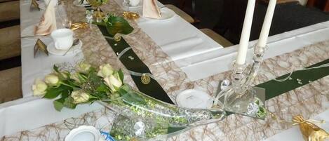 Una larga mesa de comedor dispuesta con platos blancos, servilletas y un centro de mesa con flores y velas.