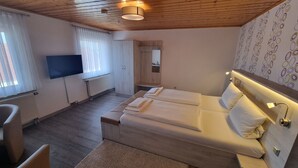 Un dormitorio moderno con techo de madera, televisor de pantalla plana, cama grande con ropa blanca, una pequeña zona de estar y pared con estampado.
