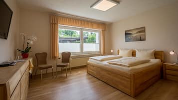 Ein Schlafzimmer mit einem hölzernen Bett, einem Schreibtisch, zwei Stühlen, einem Heizkörper und einem Fenster mit Vorhängen.