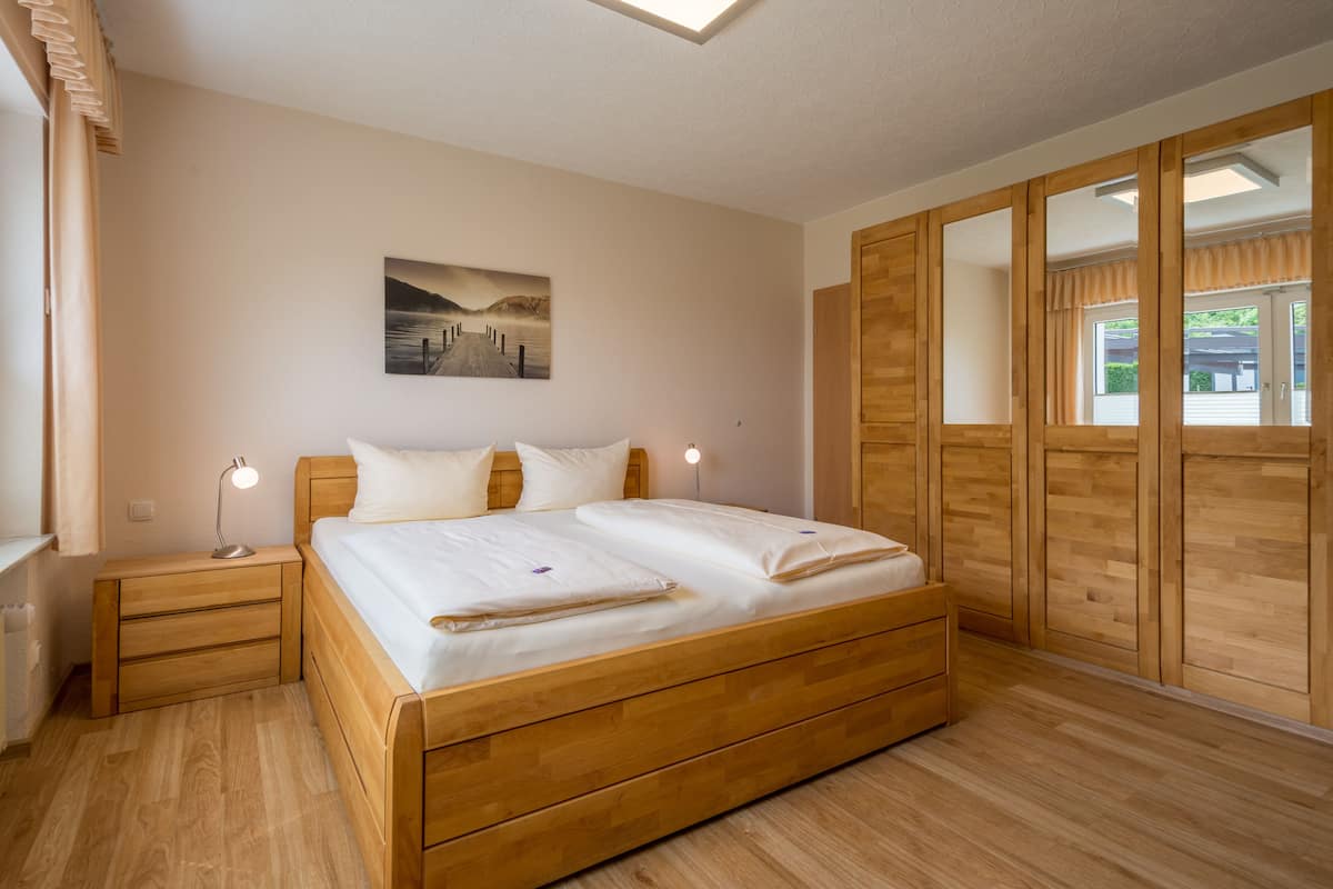 A bedroom with a wooden bed, nightstands, a bedside lamp, and a large window with curtains.