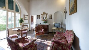 A room with a large window, a wooden ceiling, a sofa, a chair, a small table, and a television. - Cosy apartment for 2 guests with A/C, pool, WIFI, TV and panoramic view (Cortona)