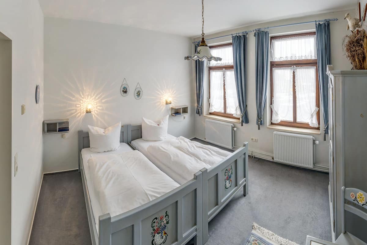 A bedroom with two beds, a radiator, and a window with curtains.