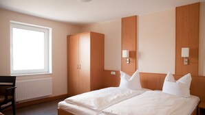 A hotel room with a large bed, wooden wardrobe, bedside lamps, and a window. - Apartmenthaus Wesertor (Kassel)