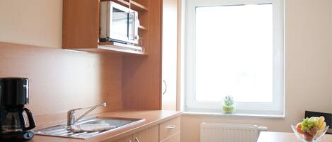 Una cocina compacta con armarios de madera, un microondas integrado y un ventanal que proporciona luz natural.