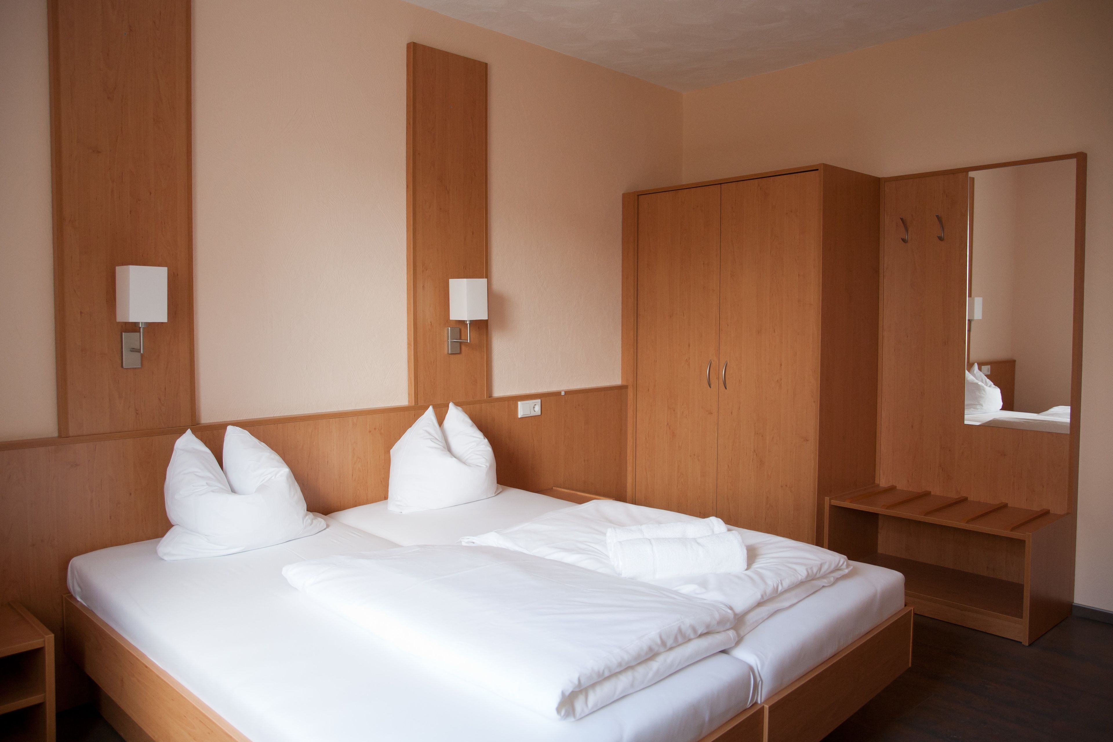 A hotel room with a large bed, wooden wardrobe, and a mirror.