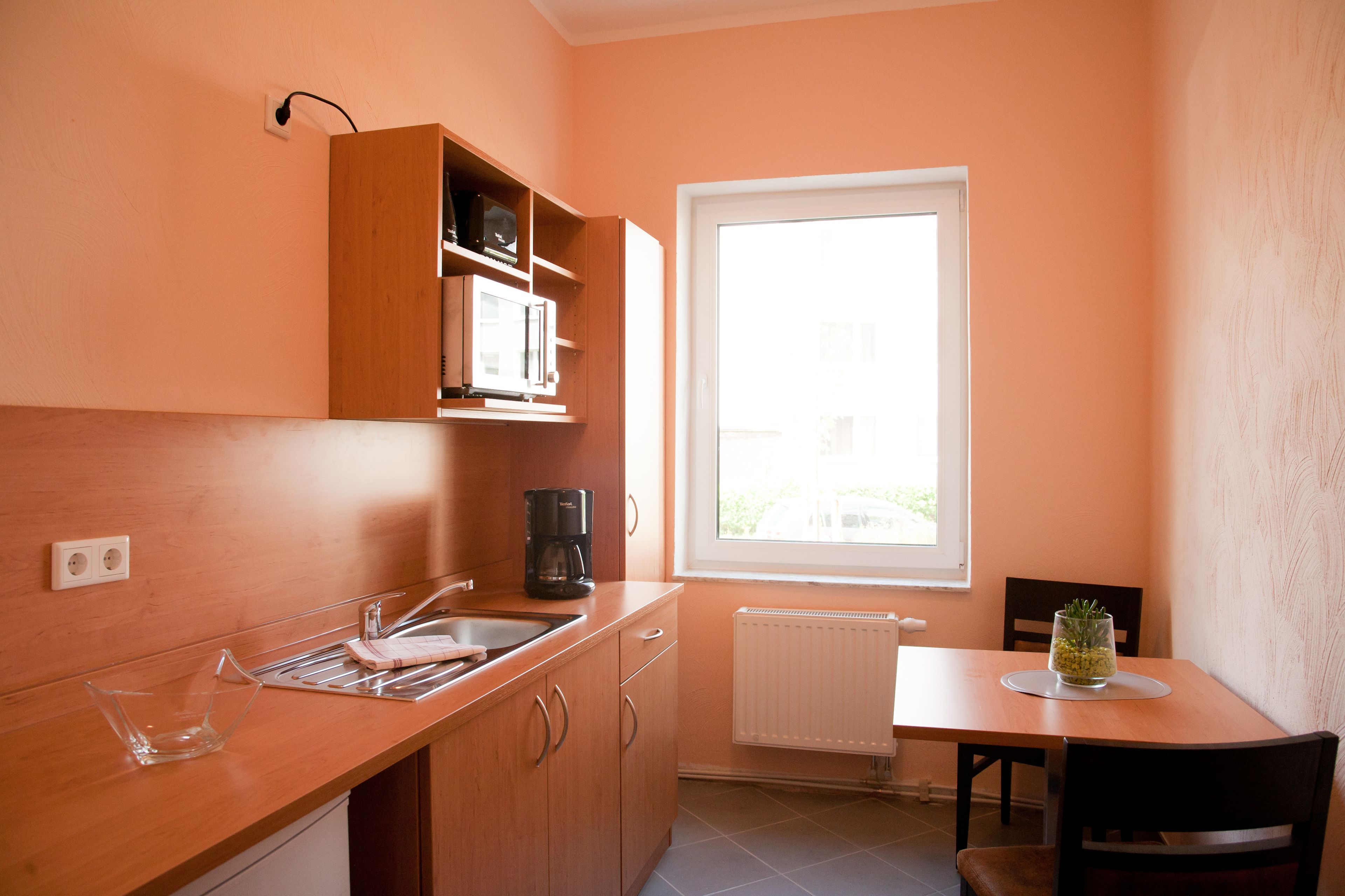 Eine kleine Küche mit Einbau-Mikrowelle, Kaffeemaschine und einem Fenster für natürliches Licht.