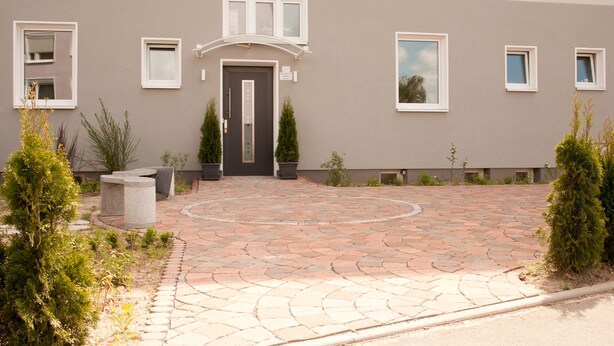 A building with a grey facade, a central entrance with a dark door, and a paved courtyard with potted plants. - Apartmenthaus Wesertor (Kassel)