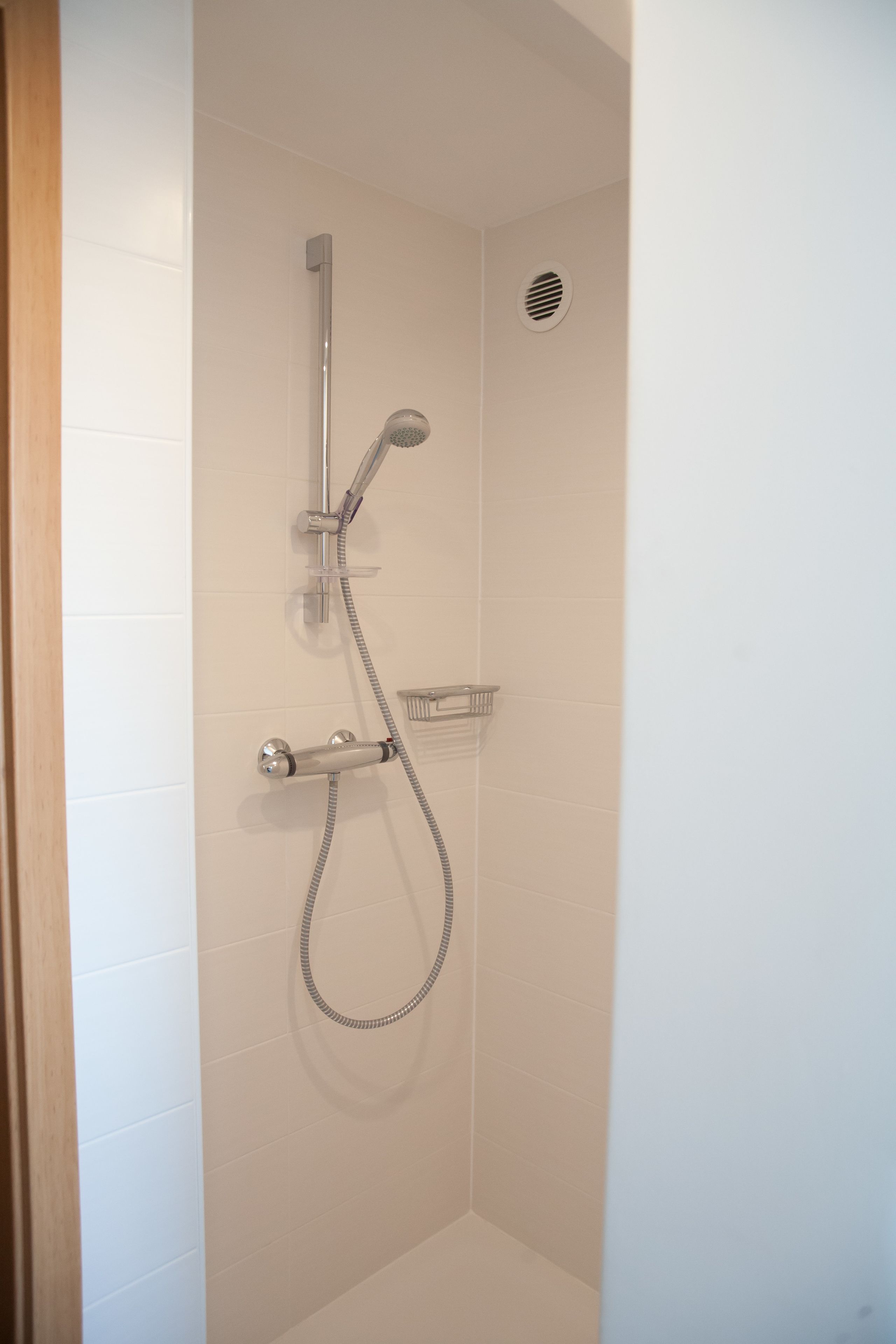A shower with a handheld showerhead and a wall-mounted faucet.
