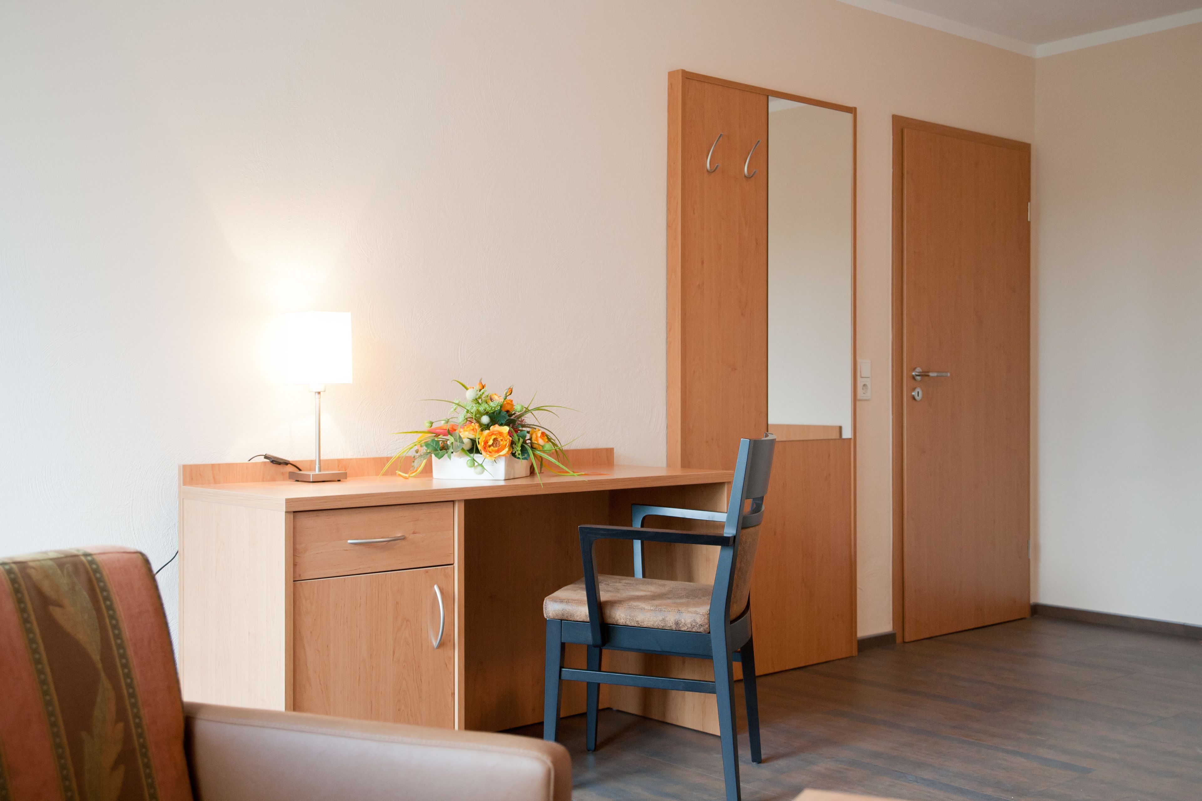 Une pièce avec un bureau en bois, une chaise, une lampe et un miroir.