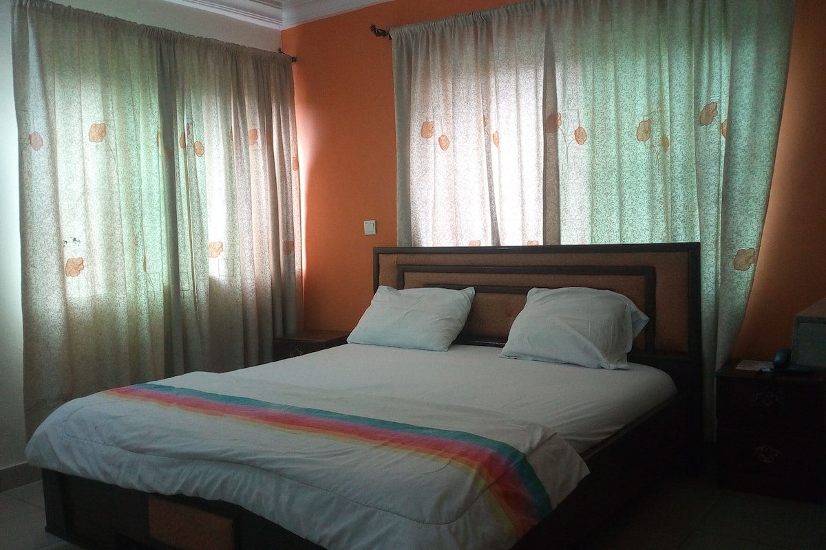 A single bed with a wooden headboard, two pillows, and a rainbow-striped blanket.