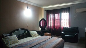 A bedroom with a bed, a chair, a desk, and a window with curtains. - Abal Hall and Hotels (Ibadan)