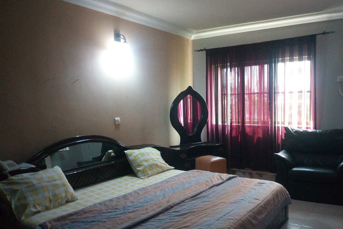 A bedroom with a bed, a chair, a desk, and a window with curtains.
