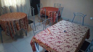 A dining area with two round tables covered with patterned tablecloths, surrounded by metal chairs. - Abal Hall and Hotels (Ibadan)