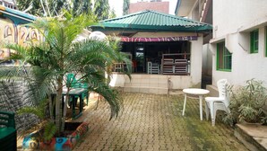 A courtyard with a paved floor, green chairs, a small table, and a building with a green roof and a sign that reads "TUAK". - Abal Hall and Hotels (Ibadan)
