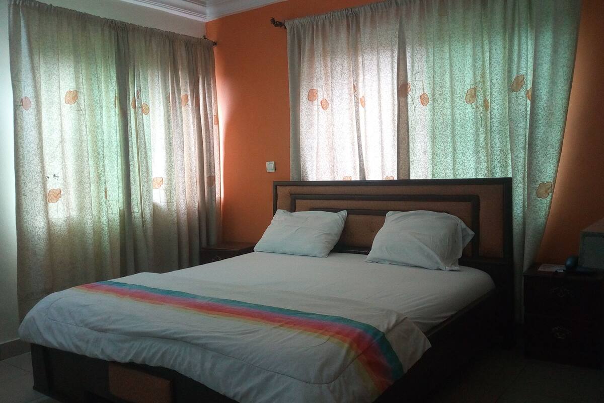 A single bed with a wooden headboard, two pillows, and a rainbow-striped blanket.
