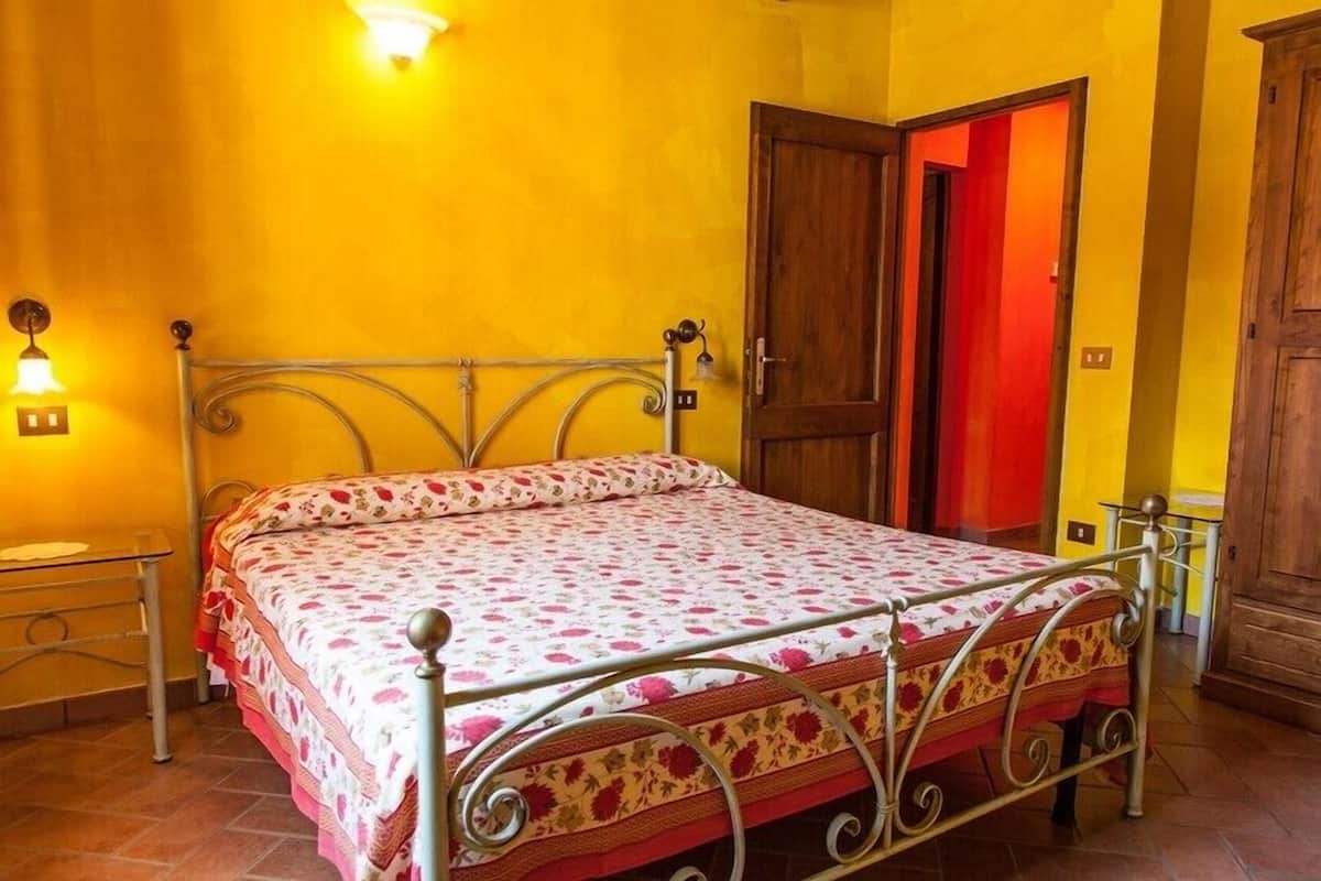 Une chambre à coucher avec un lit en métal, une table de chevet, une commode et une porte en bois.